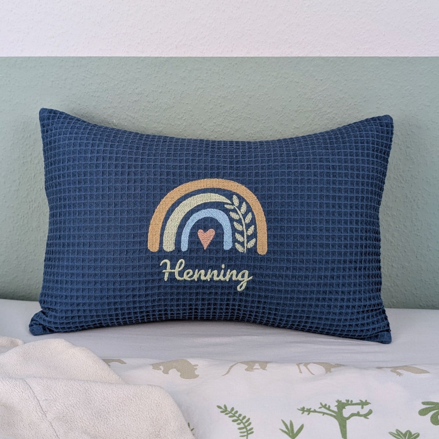 Kissen in der Größe 25 x 40 cm aus einem Waffelstoff in der Farbe blau. Mittig bestickt mit einem Regenbogen. Darunter steht ein Name.