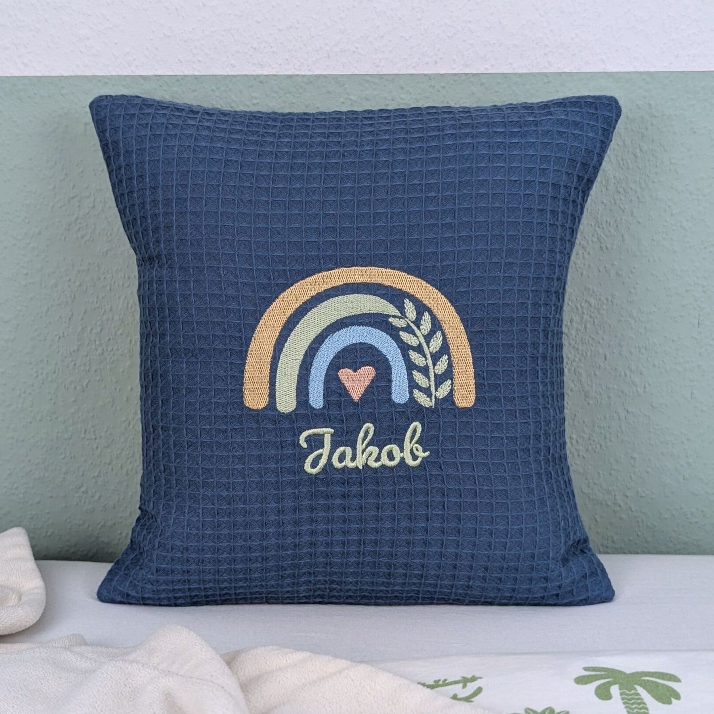 Kissen in der Größe 30 x 30 cm, aus Waffelstoff in der Farbe blau, bestickt mit einem Regenbogen und darunter steht mittig eine Name.