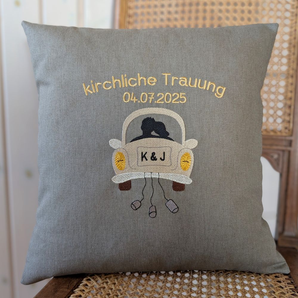 Kissen aus einem festen Baumwollstoff bestickt mit dem Schriftzug "kirchliche Trauung" und darunter das Hochzeitsdatum. Das Motiv ist ein Hochzeitsauto on hinten mit einem Brautpaar als Umriss. Auf dem Kennzeichen sind Initialen K&J gestickt.