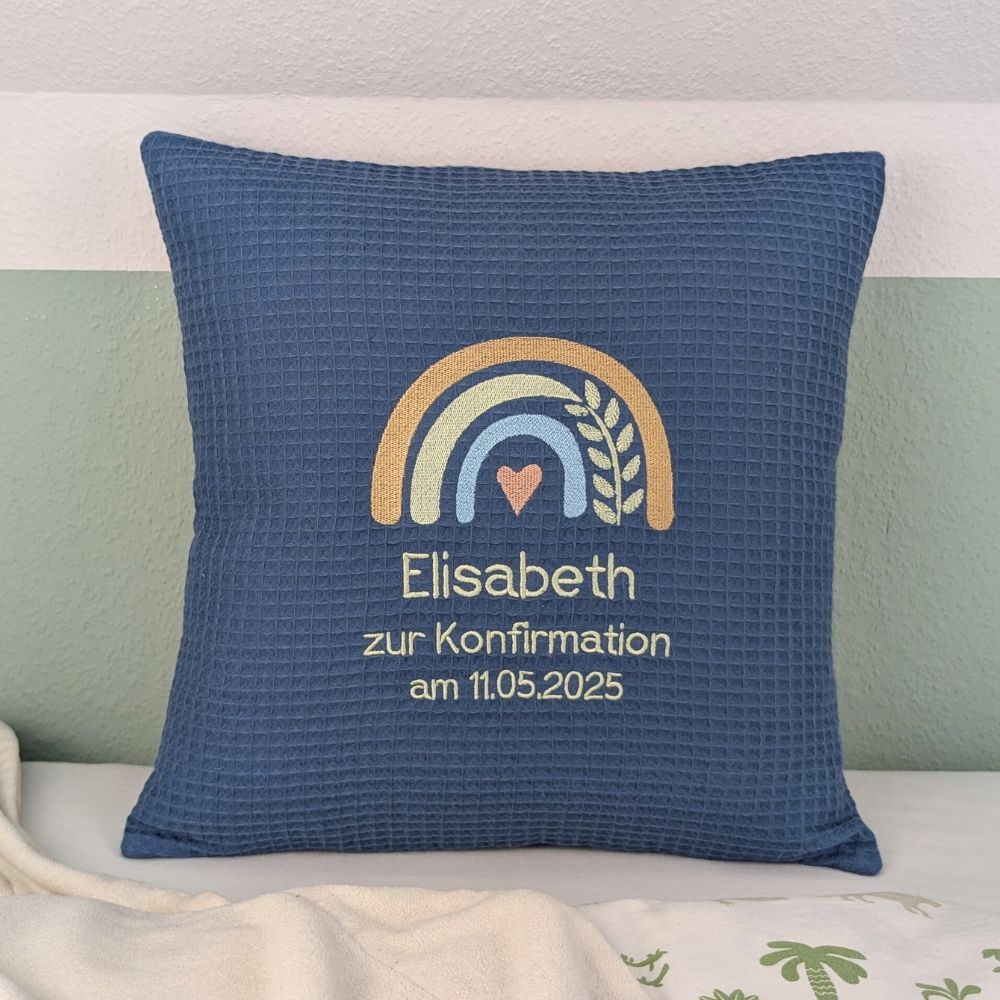 Quadratisches Kissen aus blauem Waffelstoff, bestickt mit Regenbogenmotiv in vier Farben. Mit Herz in der Mitte und Ranke. Bestickt mit Name, zur Konfirmation und Datum.