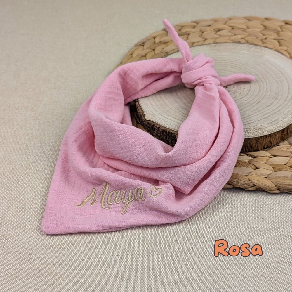 Es ist ein Halstuch aus Musselin bestickt mit  Name und einem kleinen Herzen hinter dem Namen zu sehen. Das Tuch hat die Farbe Rosa.
