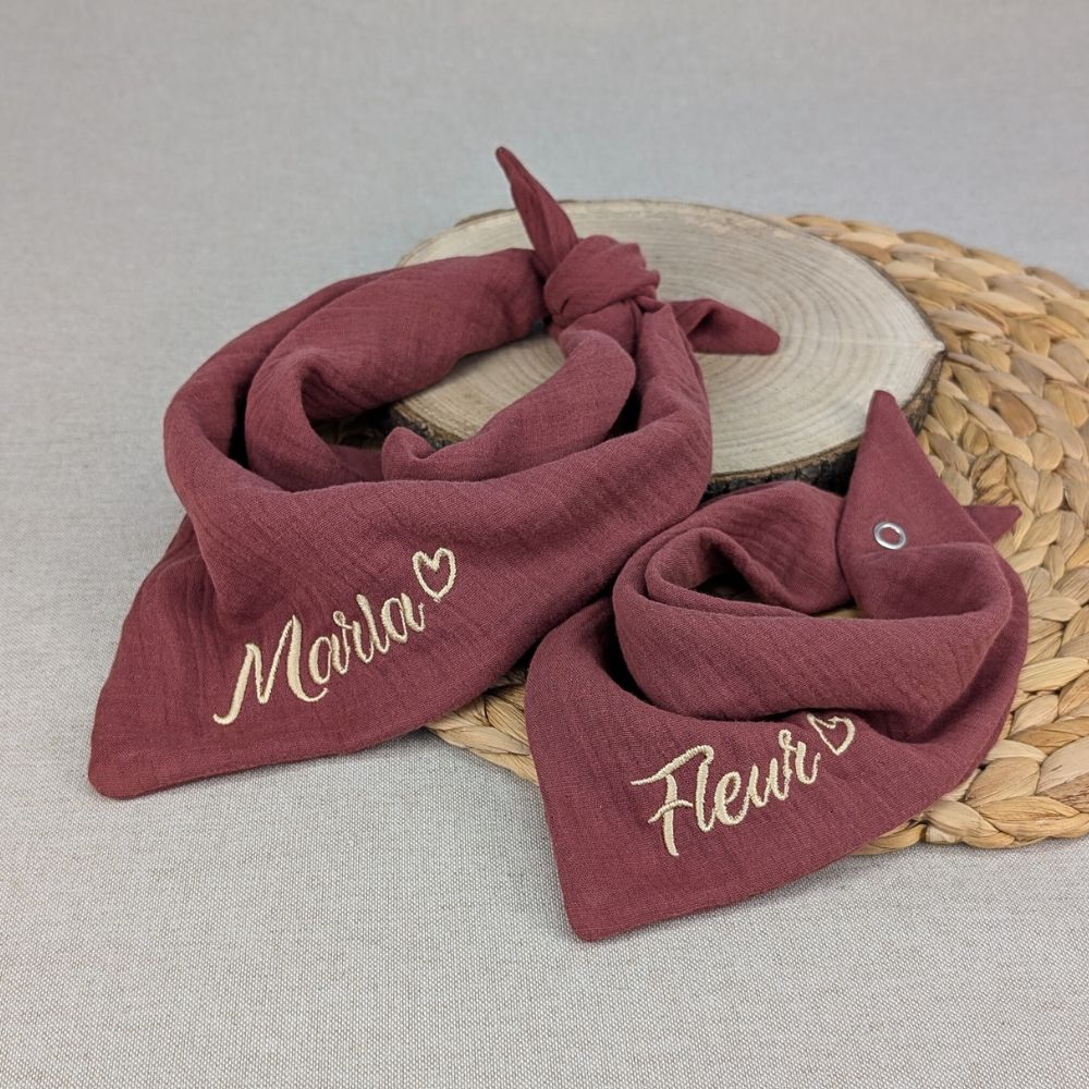 Es sind zwei Halstücher aus Musselin bestickt mit Namen und einem kleinen Herzen hinter dem Namen. Die Tücher hat die Farbe rouge.