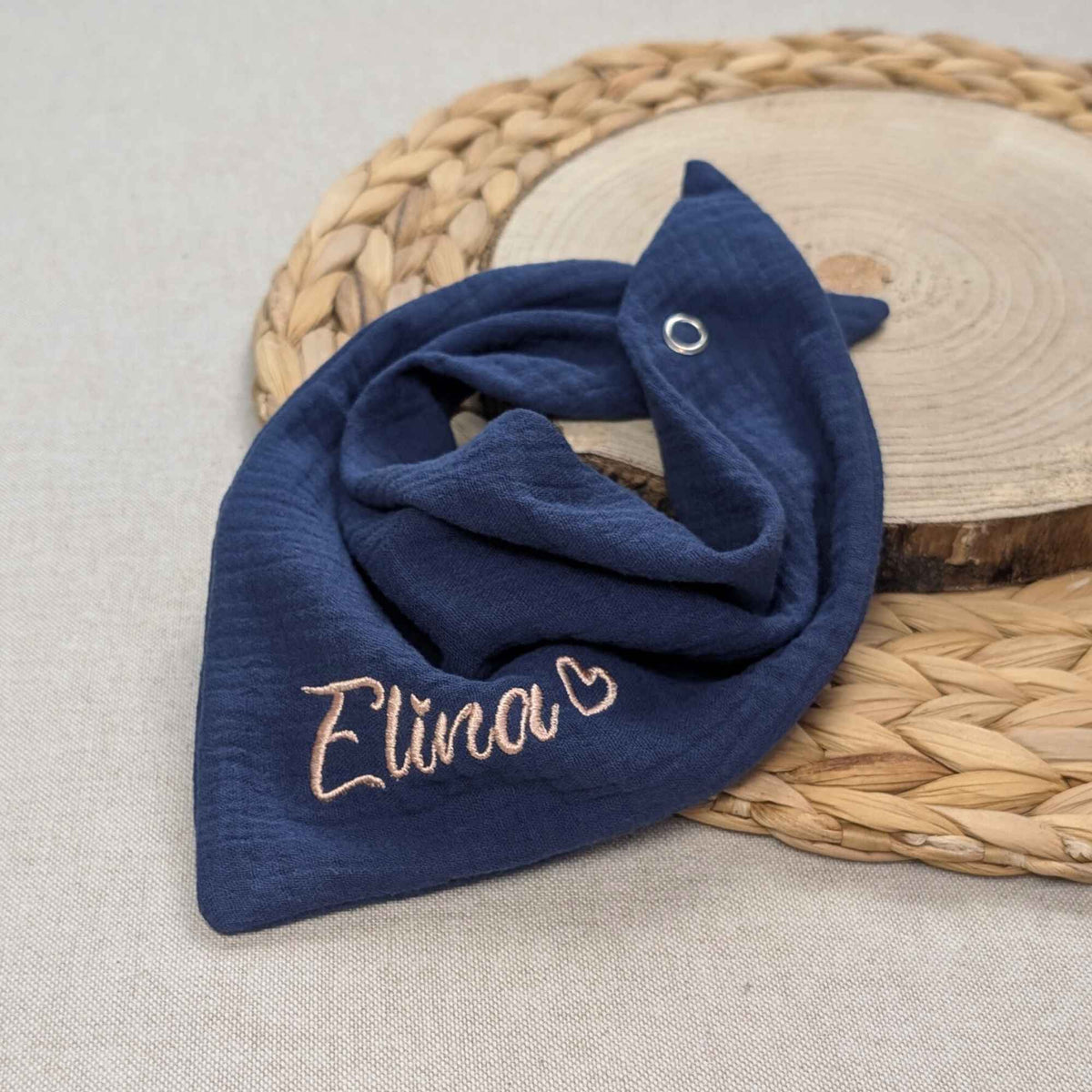 Es ist ein Halstuch aus Musselin bestickt mit dem Namen Elina und einem kleinen Herzen hinter dem Namen zu sehen. Das Tuch hat die Farbe blau.