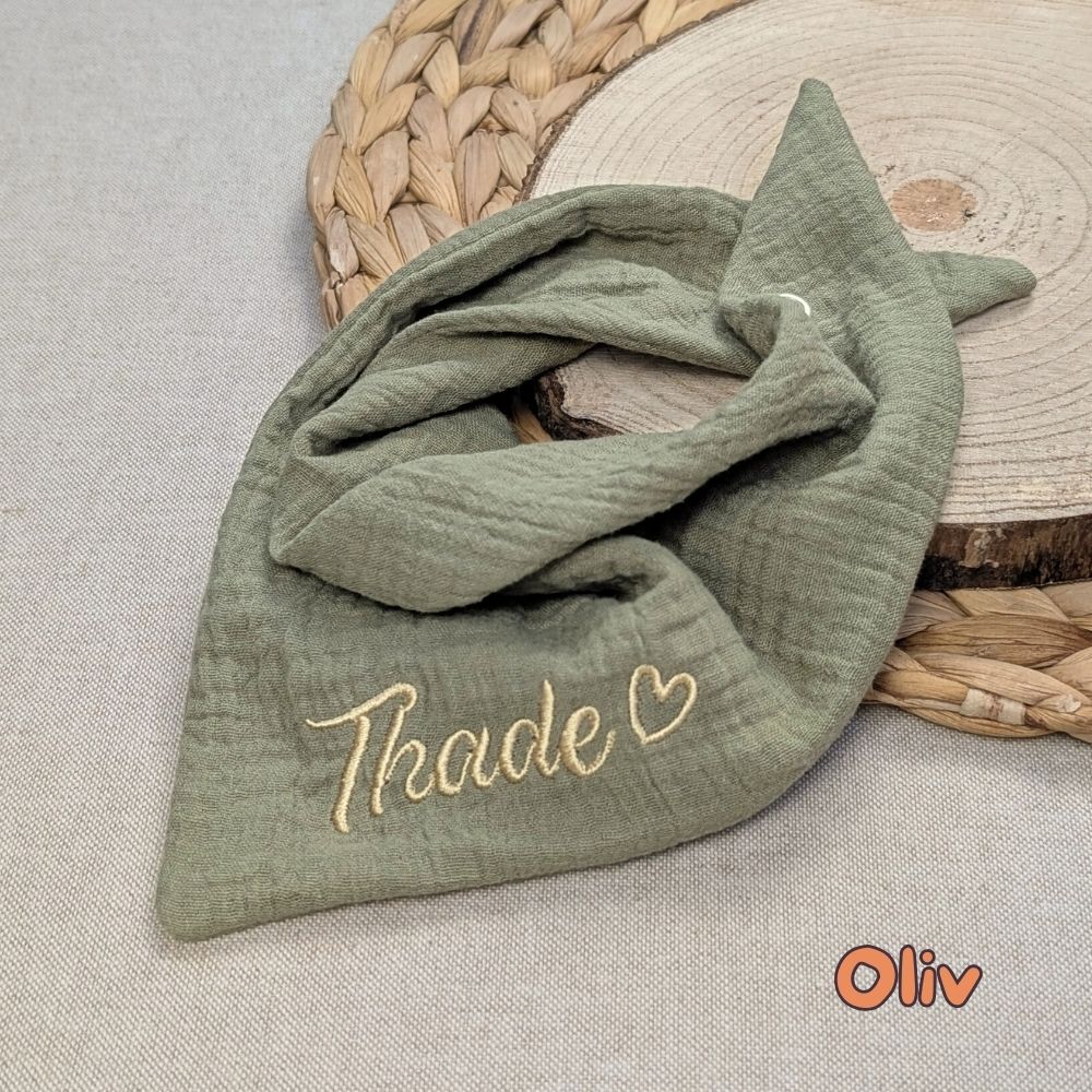 Es ist ein Halstuch aus Musselin bestickt mit dem Namen Nami und einem kleinen Herzen hinter dem Namen zu sehen. Das Tuch hat die Farbe Oliv.