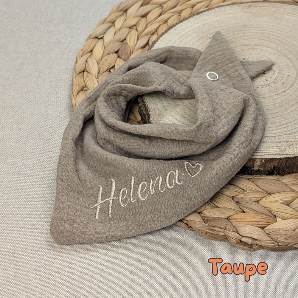 Es ist ein Halstuch aus Musselin bestickt mit dem Namen Helena und einem kleinen Herzen hinter dem Namen zu sehen. Das Tuch hat die Farbe taupe.