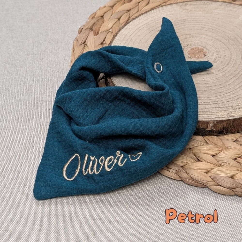 Es ist ein Halstuch aus Musselin bestickt mit  Name und einem kleinen Herzen hinter dem Namen zu sehen. Das Tuch hat die Farbe Petrol.