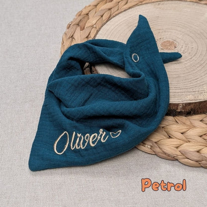 Es ist ein Halstuch aus Musselin bestickt mit  Name und einem kleinen Herzen hinter dem Namen zu sehen. Das Tuch hat die Farbe Petrol.