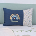 Personalisiertes Kissen mit Name. Das Kissen hat eine blaue Waffelstoff-Seite mit einer Stickerei eines Regenbogens in Gold, Grün und Blau, ergänzt durch ein Herz- und Ährenmotiv. Darunter ist der Name in grüner Schrift gestickt. Die rechte Seite des Kissens besteht aus einem gemusterten Stoff.