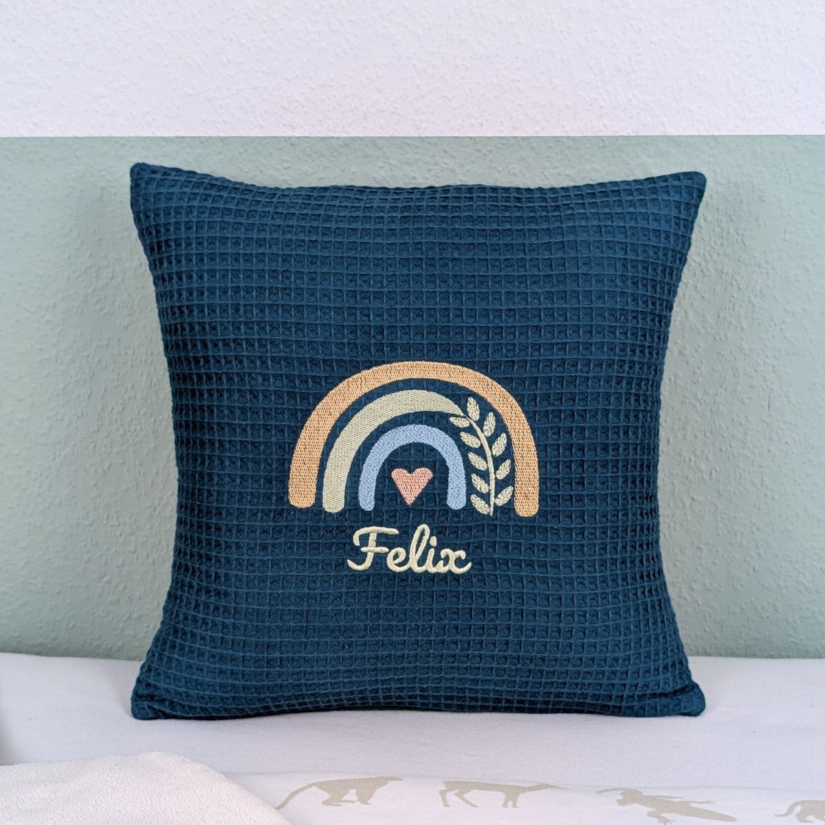 Kissen in der Größe 30 x 30 cm, aus Waffelstoff in der Farbe petrol, bestickt mit einem Regenbogen und darunter steht mittig eine Name.
