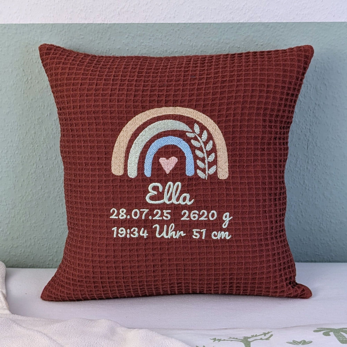Kissen in der Größe 30 x 30 cm, aus Waffelstoff in der Farbe Rost, bestickt mit einem Regenbogen und darunter steht mittig eine Name. Unter dem Namen stehen in zwei Zeilen Geburtsdaten
