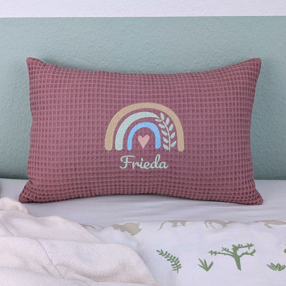 Kissen in der Größe 25 x 40 cm aus einem Waffelstoff in der Farbe altsosa. Mittig bestickt mit einem Regenbogen. Darunter steht ein Name. 