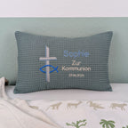 Rechteckiges Kissen in türkiser Farbe mit Waffelstruktur liegt auf einem Bett. Auf dem Kissen sind ein gesticktes Kreuz und ein christliches Ichthys-Symbol (Fisch) sowie der Text „Sophie – Zur Kommunion – 27.4.2025“ in verschiedenen Farben eingestickt. Das Kissen dient als personalisiertes Geschenk zur Erstkommunion.