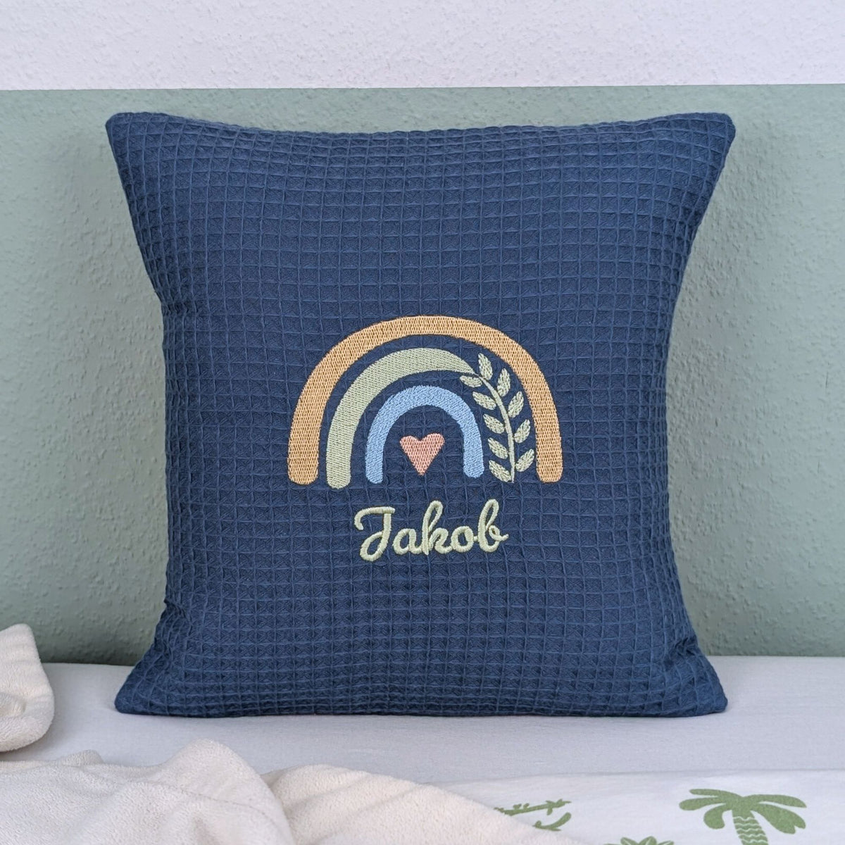 Kissen in der Größe 30 x 30 cm, aus Waffelstoff in der Farbe blau, bestickt mit einem Regenbogen und darunter steht mittig eine Name. 