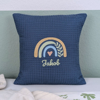 Kissen in der Größe 30 x 30 cm, aus Waffelstoff in der Farbe blau, bestickt mit einem Regenbogen und darunter steht mittig eine Name. 
