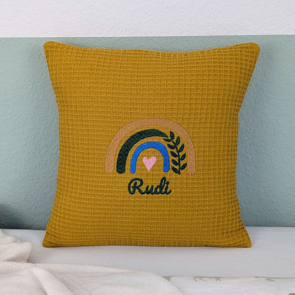 Kissen in der Größe 30 x 30 cm, aus Waffelstoff in der Farbe ocker, bestickt mit einem Regenbogen und darunter steht mittig eine Name.