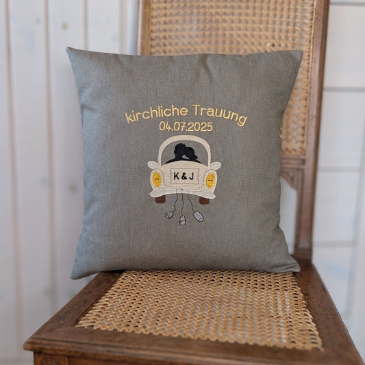Kissen aus einem festen Baumwollstoff bestickt mit dem Schriftzug "kirchliche Trauung" und darunter das Hochzeitsdatum. Das Motiv ist ein Hochzeitsauto on hinten mit einem Brautpaar als Umriss. Auf dem Kennzeichen sind Initialen  K&J gestickt.