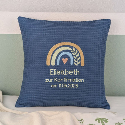 Quadratisches Kissen aus blauem Waffelstoff, bestickt mit Regenbogenmotiv in vier Farben. Mit Herz in der Mitte und Ranke. Bestickt mit Name, zur Konfirmation und Datum.  